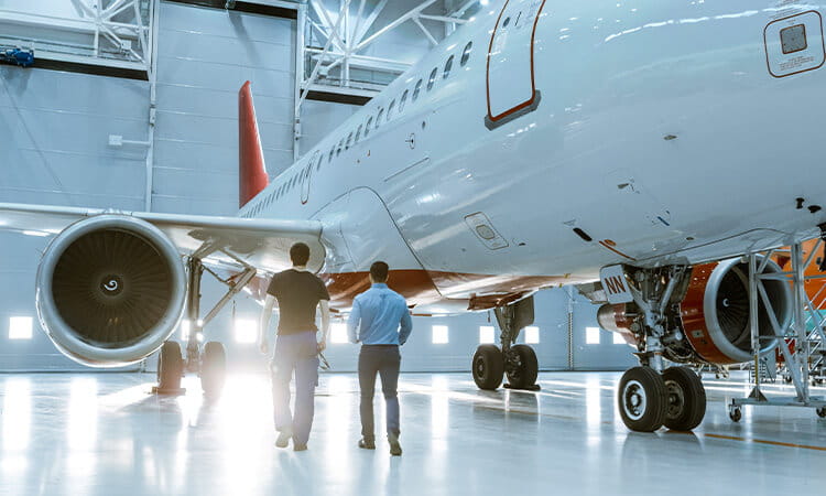 Two man walking around a plane in a hanger.