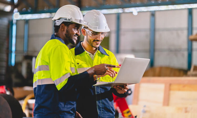 Two men in high vis tops looking at a laptop while in a shed. 