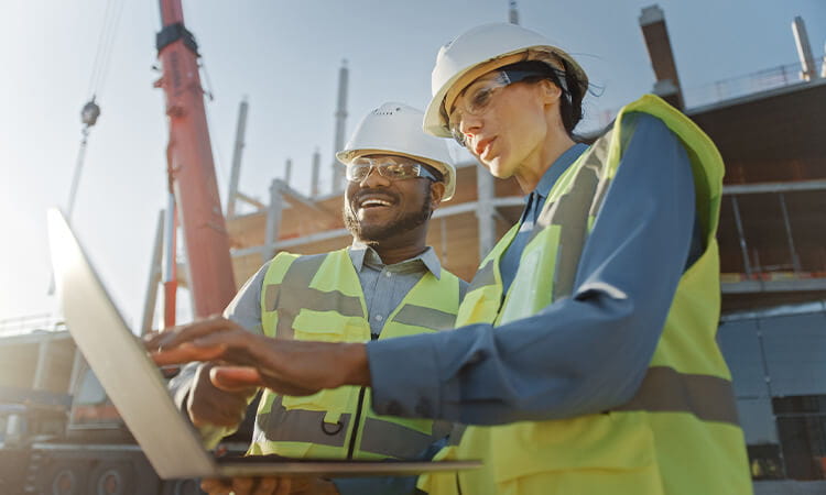 Two people on a construction site working on a laptop.