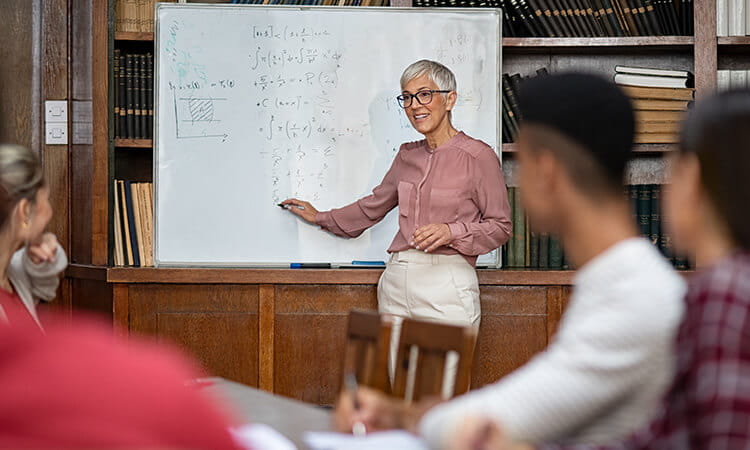 A lady teaching students maths from a whiteboard. 