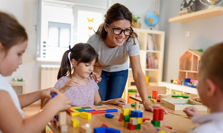 An early childhood teacher helping children play with blocks. 