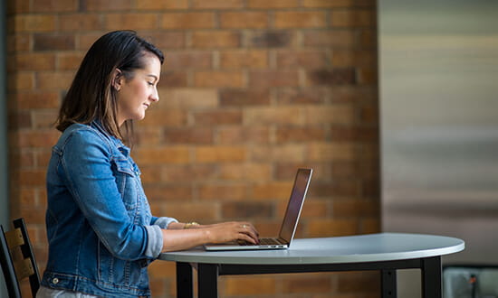 Female sitting at desk typing on laptop.