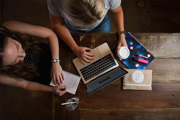 Students sitting at desk, using laptop and writing notes. 