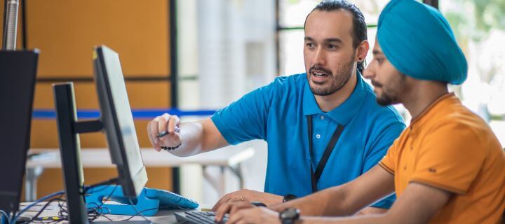 Two men working together at a computer in an office setting.