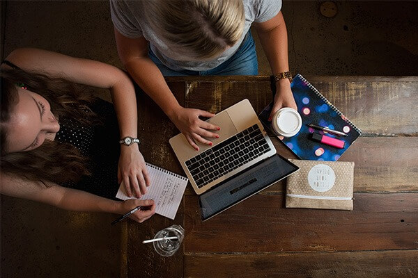 Two students sitting at a desk, looking at a laptop.