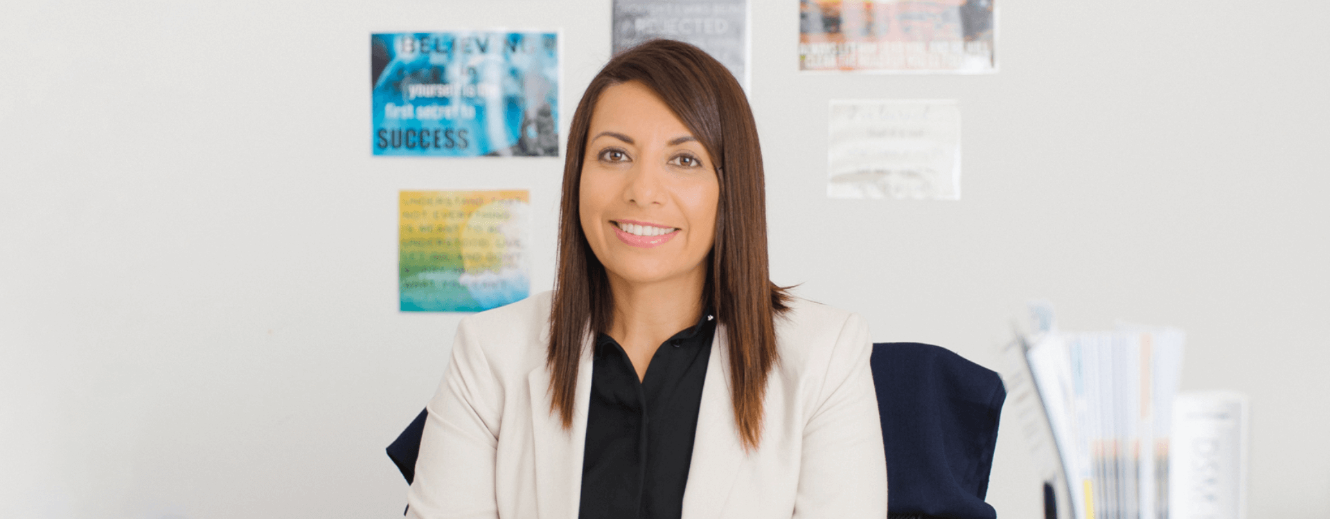 Lady in white jacket and business shirt in an office with motivational posters on the wall.