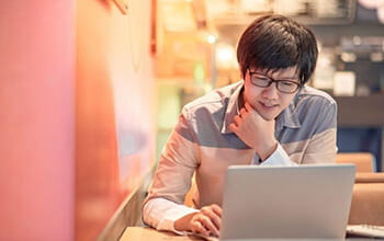 Young man concentrating on laptop in a warmly lit indoor setting.