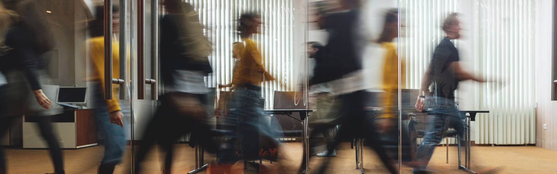 Busy office in motion with a group of people walking past a conference room.