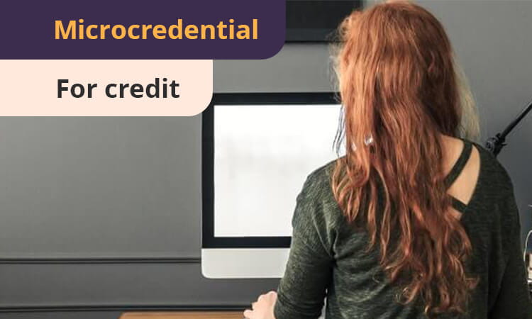 Person with long red hair sitting at a desk using a computer screen. Text at the top reads "Microcredential for credit.
