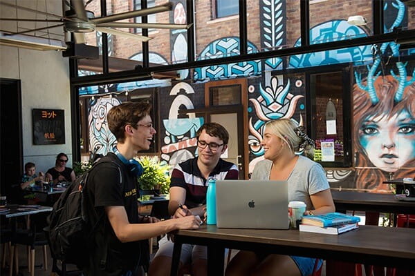 A group of students working together on a laptop, in a cafe. 