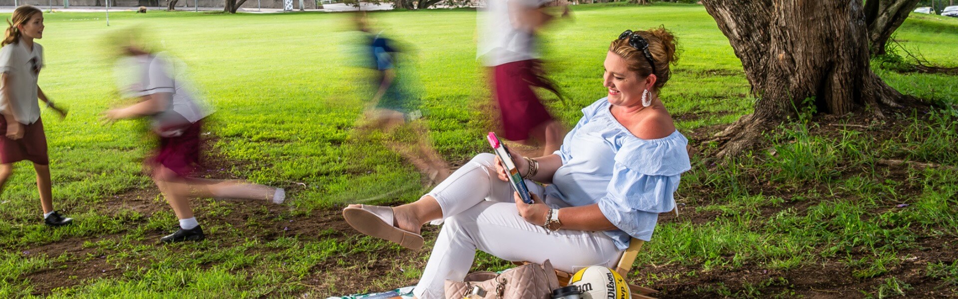 A lady appearing to be studying in a park with her children playing around her.