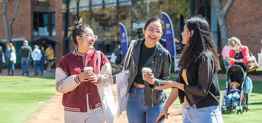 Three students walking in on-campus quadrangle holding coffee cups
