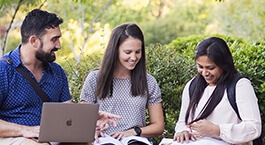 Three students studying together with books and a laptop.