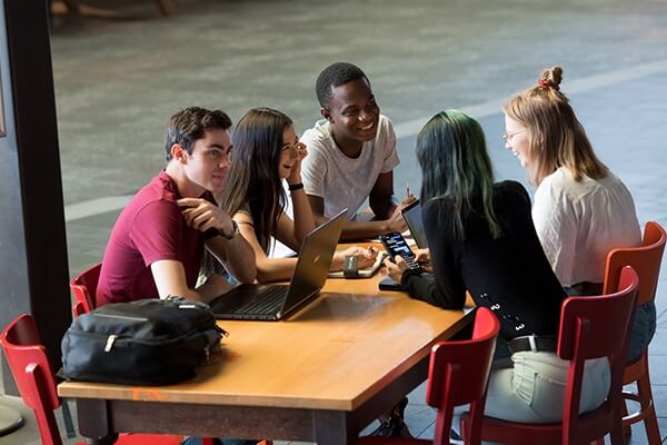 Group of five students sitting at table outside cafe.