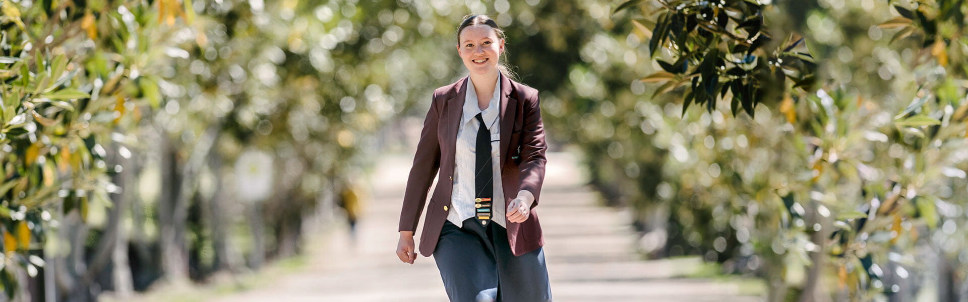 Female high school student walking in a park, smiling at the camera.