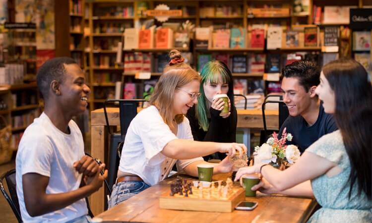 A group of young students, sitting at a table, drinking coffee while in conversation.