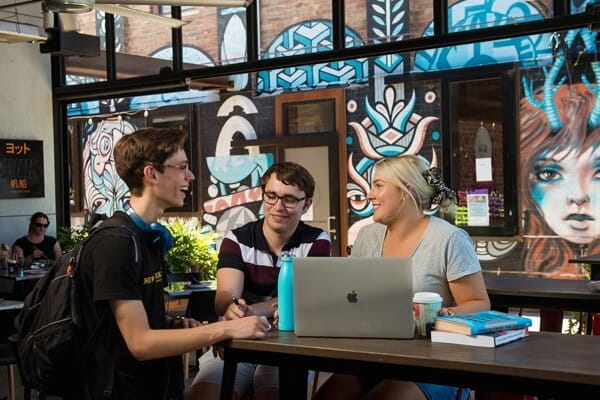 3 students sitting at a cafe, chatting and studying.