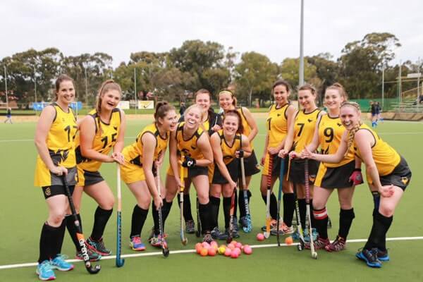 A female hockey team on the field, smiling after winning the game.