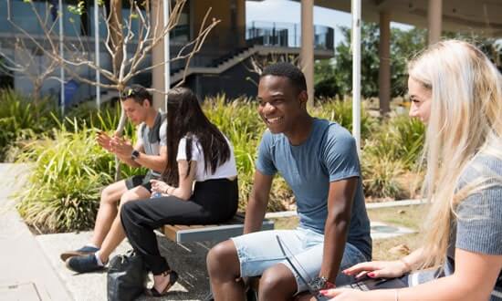 Four young people sitting outside on a timber bench, chatting and smiling.