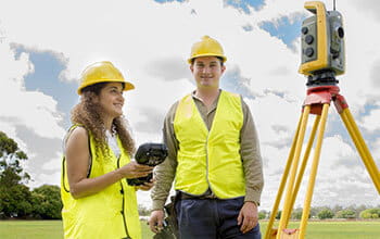 Two surveyors with a theodolite on a tripod outdoors.
