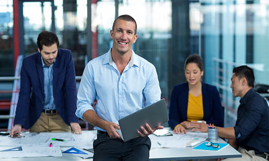 A group of professionals working at a desk with one man smiling at the camera. 