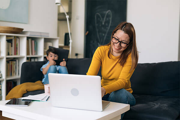 Female at laptop with male child on couch in background
