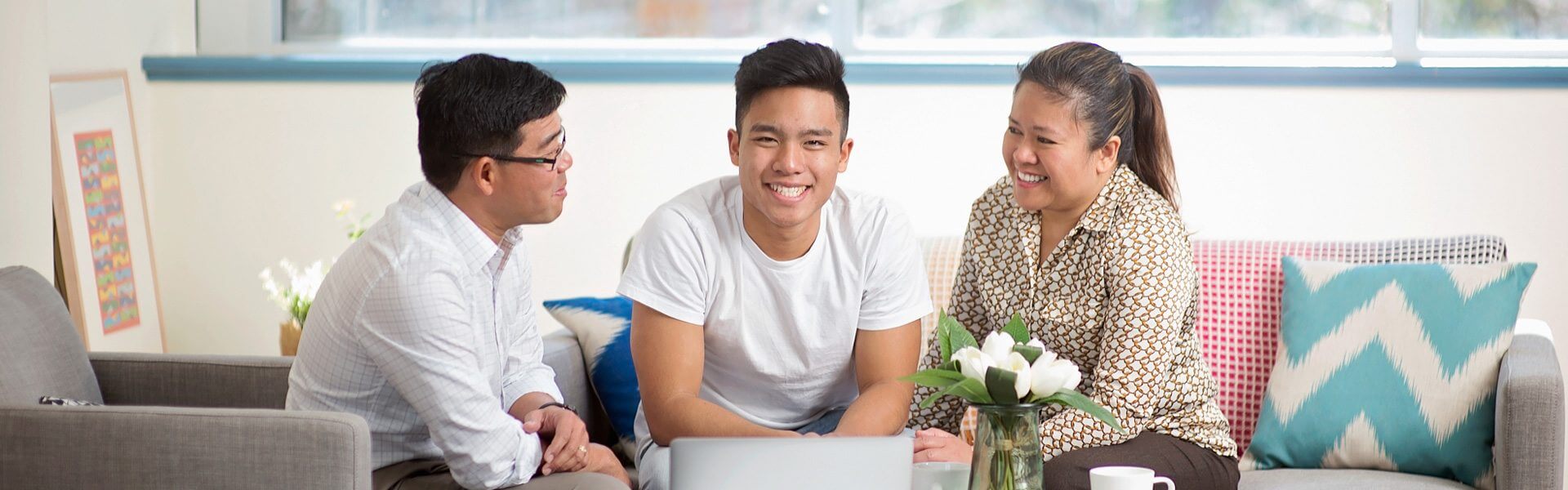 A high school student sits with his parents on a couch, smiling at the camera.