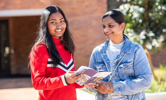 Two woman standing outdoors smiling while looking at a booklet.