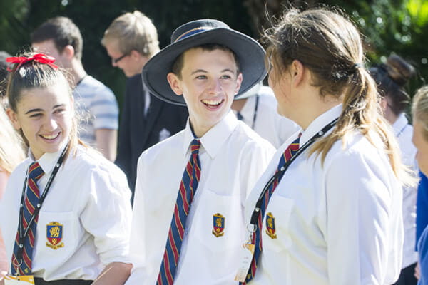 3 high school students in uniform, interacting and smiling.