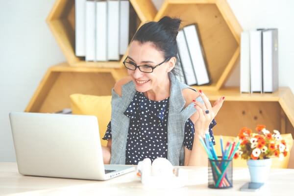 A middle age female, sitting at a desk working on her computer and smiling.