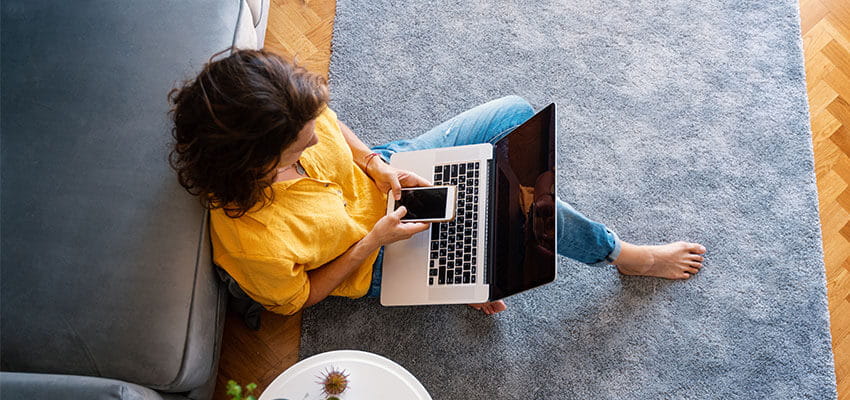 Woman sitting on loungeroom floor with laptop and mobile phone