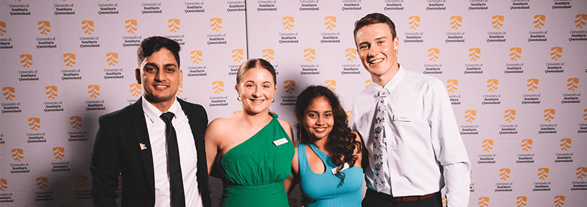 Four people smiling and standing in front of a University of Southern Queensland backdrop.
