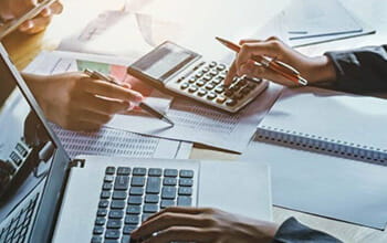 Professionals working on financial calculations with a calculator, documents, and a laptop.