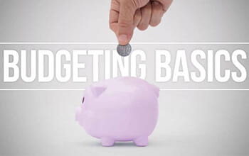A hand inserting a coin into a purple piggy bank with the words "budgeting basics" displayed above.