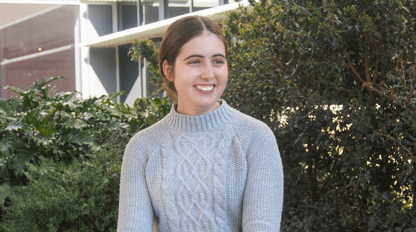 UniSQ student sitting in front of a green hedge