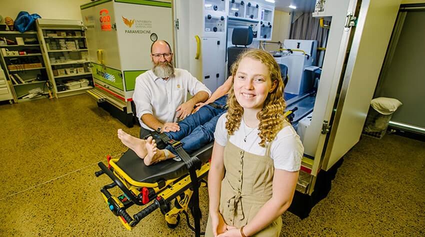 Aneka is standing in UniSQ's Paramedic Simulation lab, smiling at the camera.