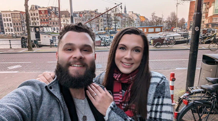 A couple posing for a selfie with a canal and bicycles in the background.