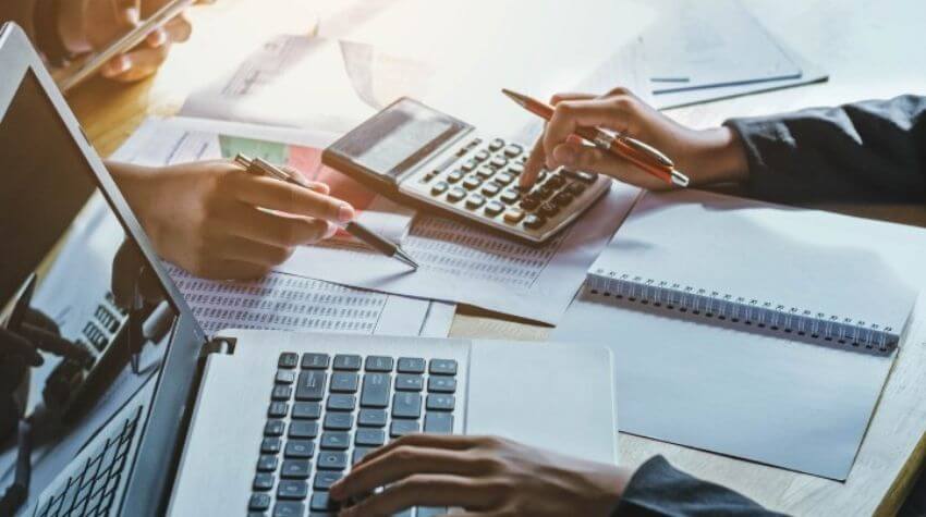 Person working on finances with calculator and laptop at a desk.