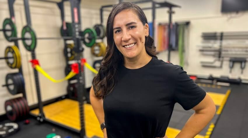 Woman smiling in a gym with exercise equipment in the background.