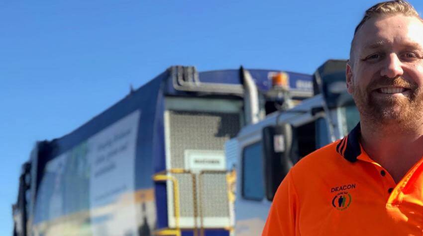 Deacon standing in front of a garbage collection vehicle, smiling at the camera.