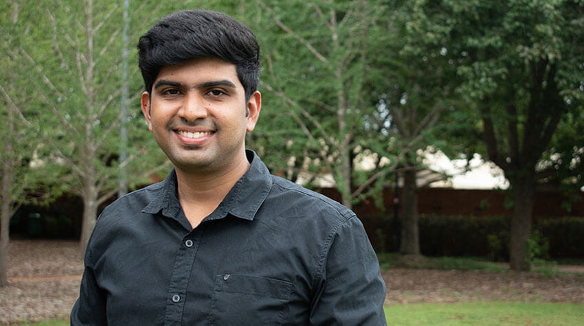 Deepak, standing outside of Z block, UniSQ Toowoomba Campus, smiling at the camera.
