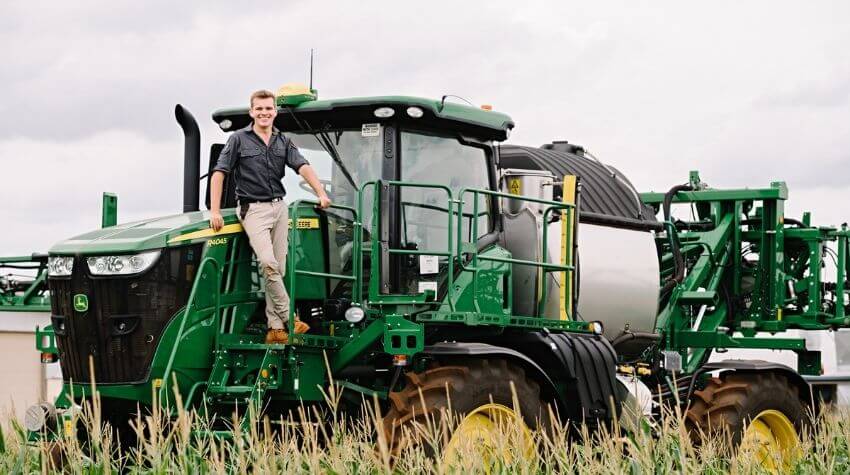 Young farmer standing on a green tractor in a field.