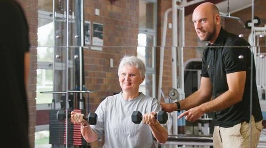 Personal trainer assisting a senior woman with dumbbell exercises.