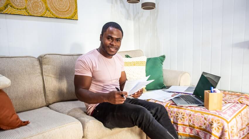 Man sitting on a sofa working with documents and a laptop.