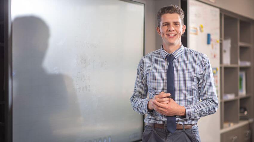Jonny standing at the front of a classroom, smiling at the camera.