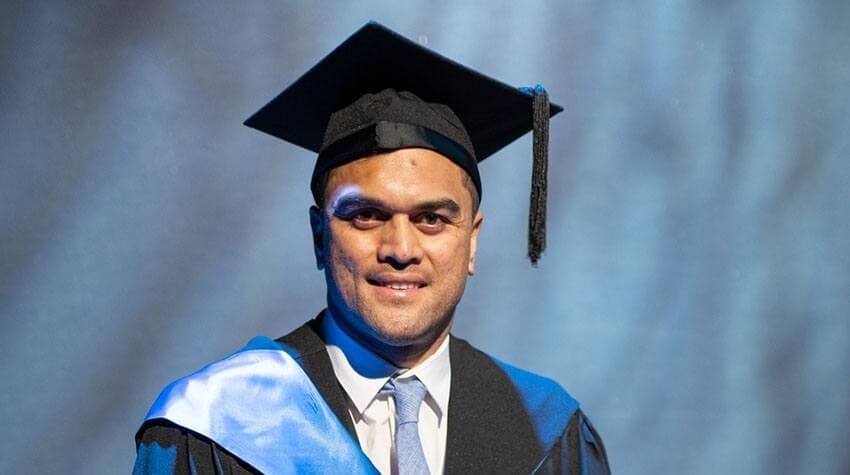 A graduate wearing a cap and gown smiles at a graduation ceremony.