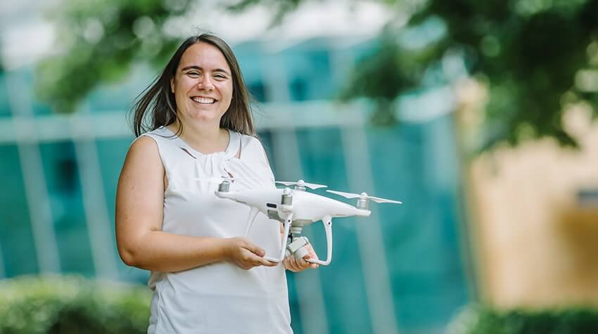 Livia is holding a white drone, in the Quad at UniSQ Toowoomba, smiling at the camera.