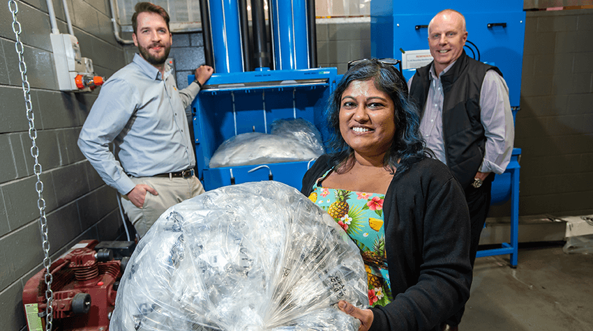 Three people. Woman at front holding a bag of rubbish.