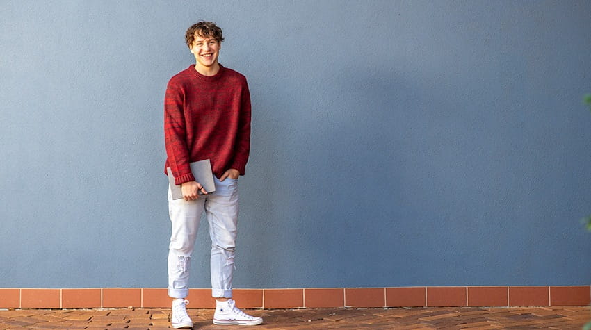 Young man smiling and standing against a blue wall with space for text.