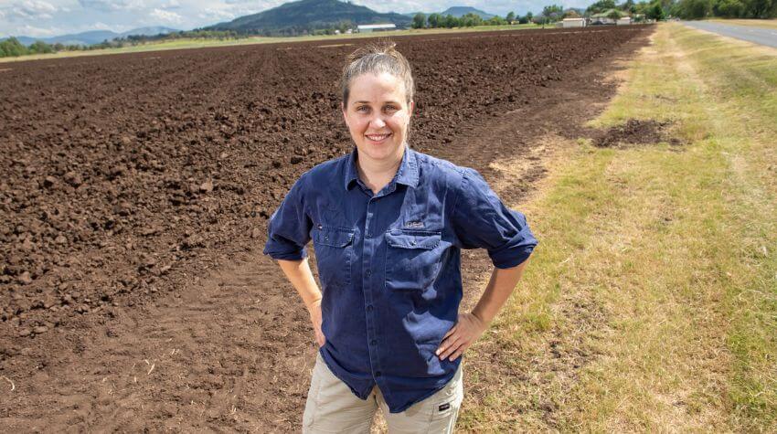 PhD student looking at the camera in front of a field